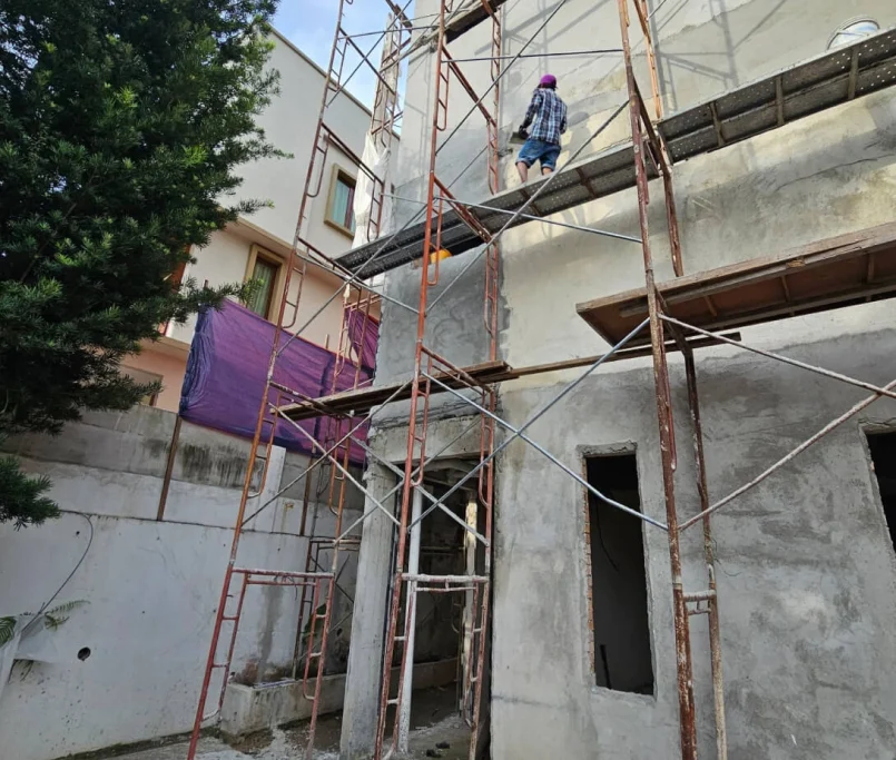 Construction worker on scaffold applying plaster to a building’s exterior wall under renovation — Project by Ray & Mist Renovation Sdn. Bhd.