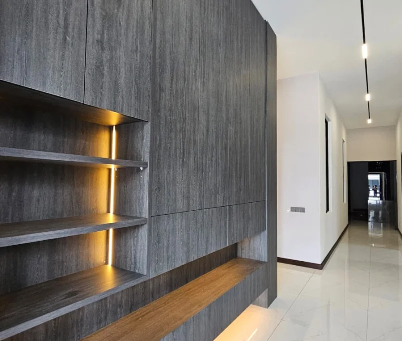 Built-in dark wood laminate cabinetry with warm LED shelf lighting and seating ledge along a modern hallway —Project by Ray & Mist Design Sdn. Bhd.