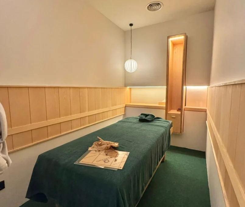 Massage treatment room with wooden panel walls, green bedding, and warm pendant lighting —Project by Ray & Mist Design Sdn. Bhd.