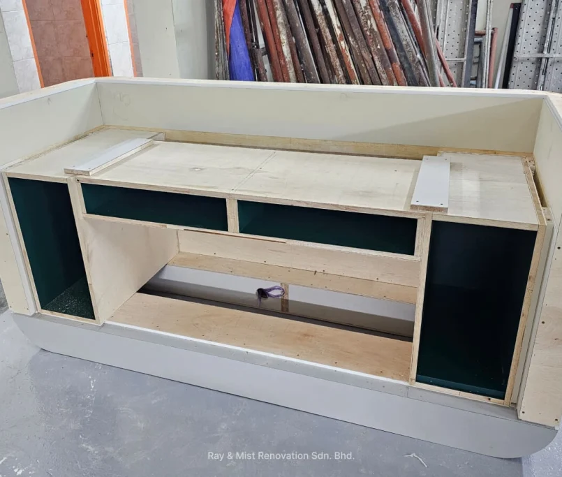 Back view of an unfinished custom-built reception counter showing open compartments and plywood framework —Project by Ray & Mist Design Sdn. Bhd.