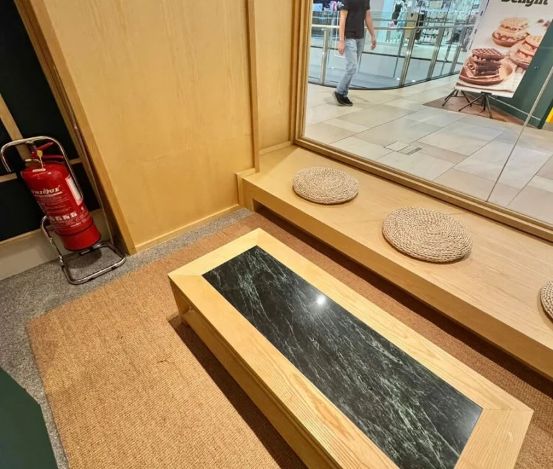 Low wooden coffee table with black marble inset, placed beside a window-facing bench with rattan seat cushions —Project by Ray & Mist Design Sdn. Bhd.