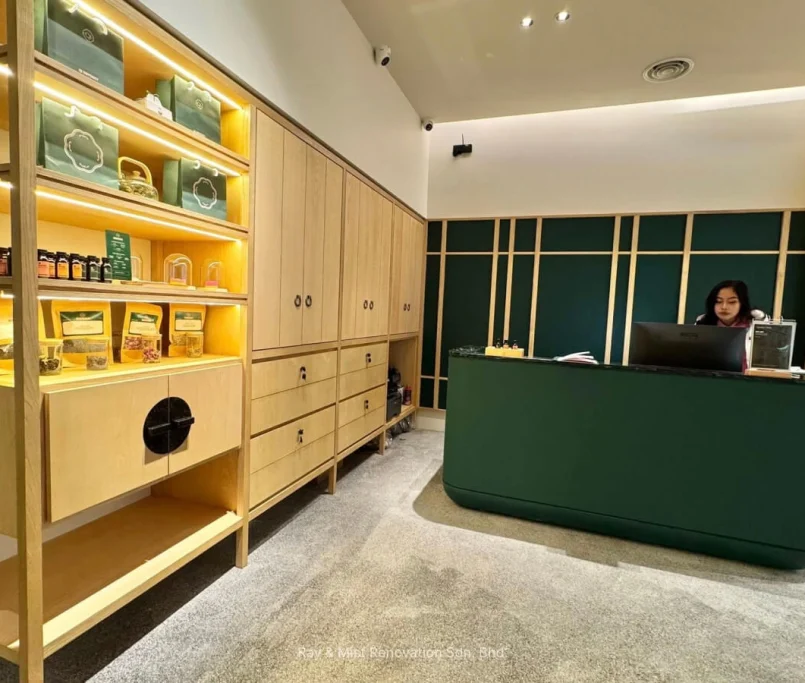 Reception area with a dark green counter and light wood display shelves showcasing wellness products —Project by Ray & Mist Design Sdn. Bhd.