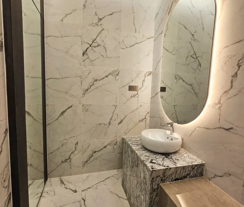 Modern bathroom with full marble walls, oval mirror, and marble basin counter — Project by Ray & Mist Renovation Sdn. Bhd.