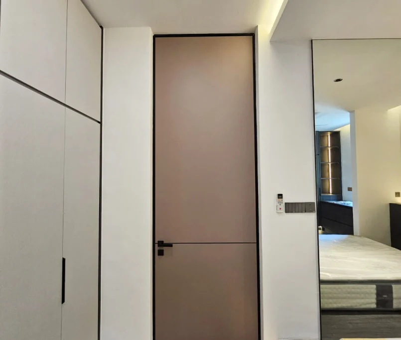 Modern bedroom with a taupe flush door, built-in wardrobe, and partial view of the bed — Project by Ray & Mist Renovation Sdn. Bhd.