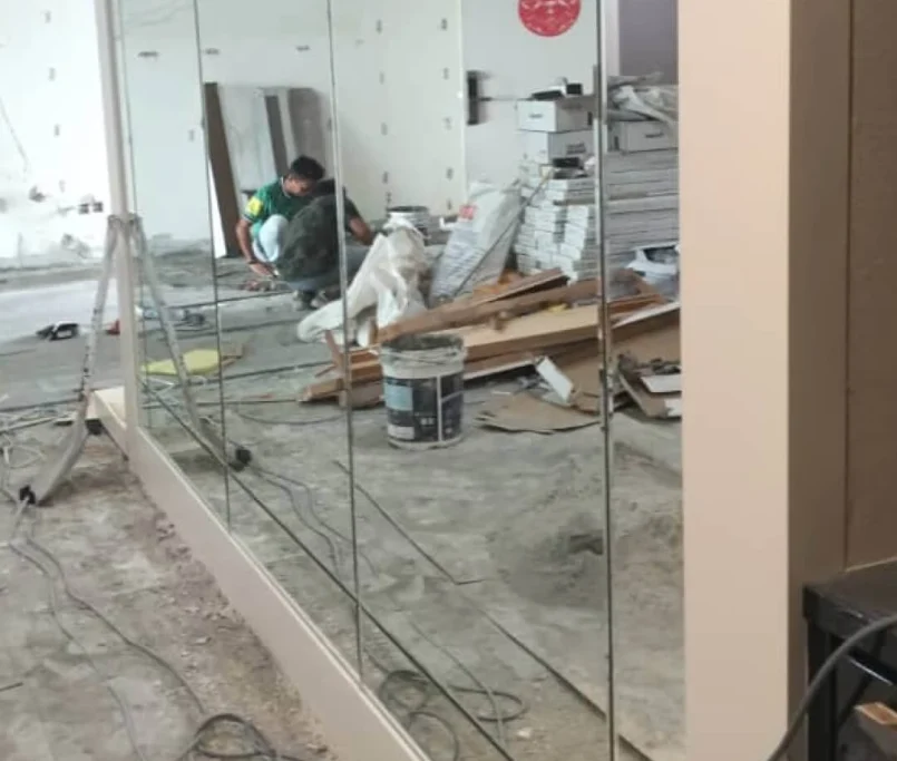 A mirror wall panel reflecting a renovation scene with construction materials, cables, and a worker on-site. —Project by Ray & Mist Renovation Sdn. Bhd.
