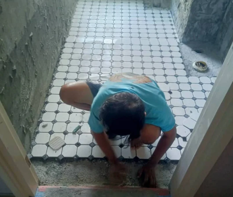 Worker installing white hexagonal bathroom floor tiles with black accents — Project by Ray & Mist Renovation Sdn. Bhd.