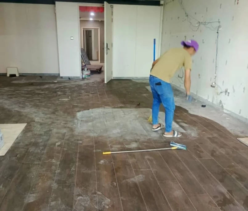 Worker cleaning newly installed dark wood-look floor tiles in a living area — Project by Ray & Mist Renovation Sdn. Bhd.